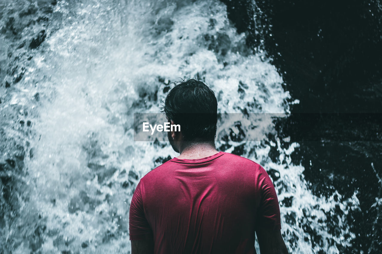 Rear view of man standing by waterfall