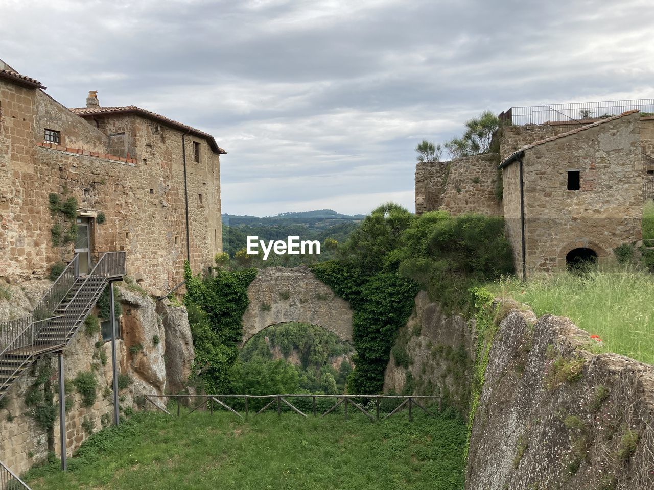 architecture, built structure, ruins, history, fortification, the past, building exterior, castle, building, village, sky, cloud, nature, wall, plant, fort, old, travel destinations, ancient history, medieval, ancient, château, stone wall, rural area, moat, no people, travel, grass, fortified wall, tourism, landscape, stone material, old ruin, land, house, rural scene, wall - building feature, outdoors, tree, residential district, day, estate, abbey, environment, surrounding wall, scenics - nature, tower