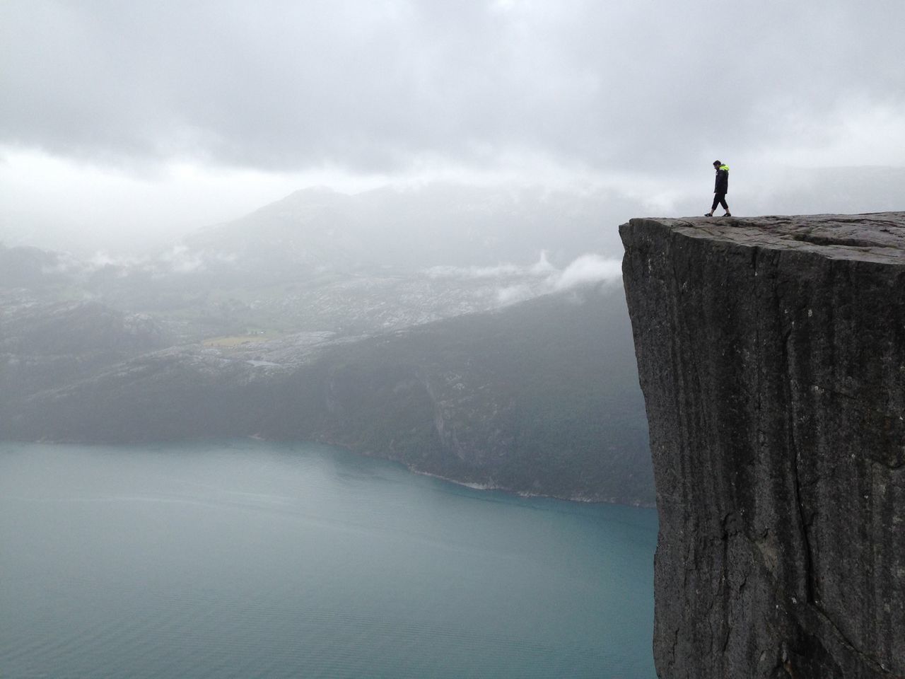 Distant view of man standing at preikestolen against cloudy sky