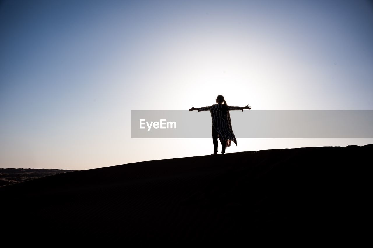 SILHOUETTE MAN WITH ARMS OUTSTRETCHED STANDING ON STREET