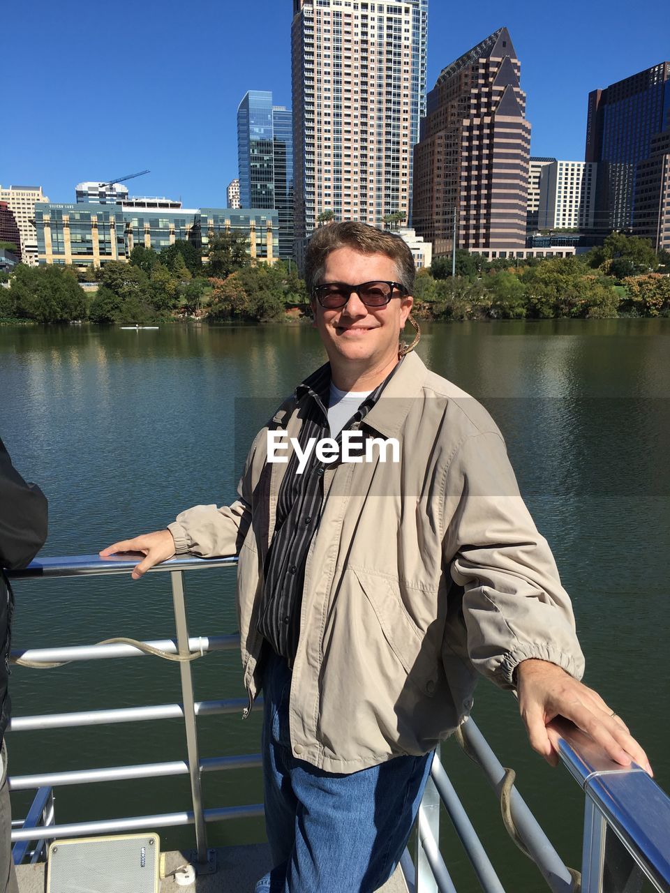 Portrait of smiling man standing by lake in city on sunny day