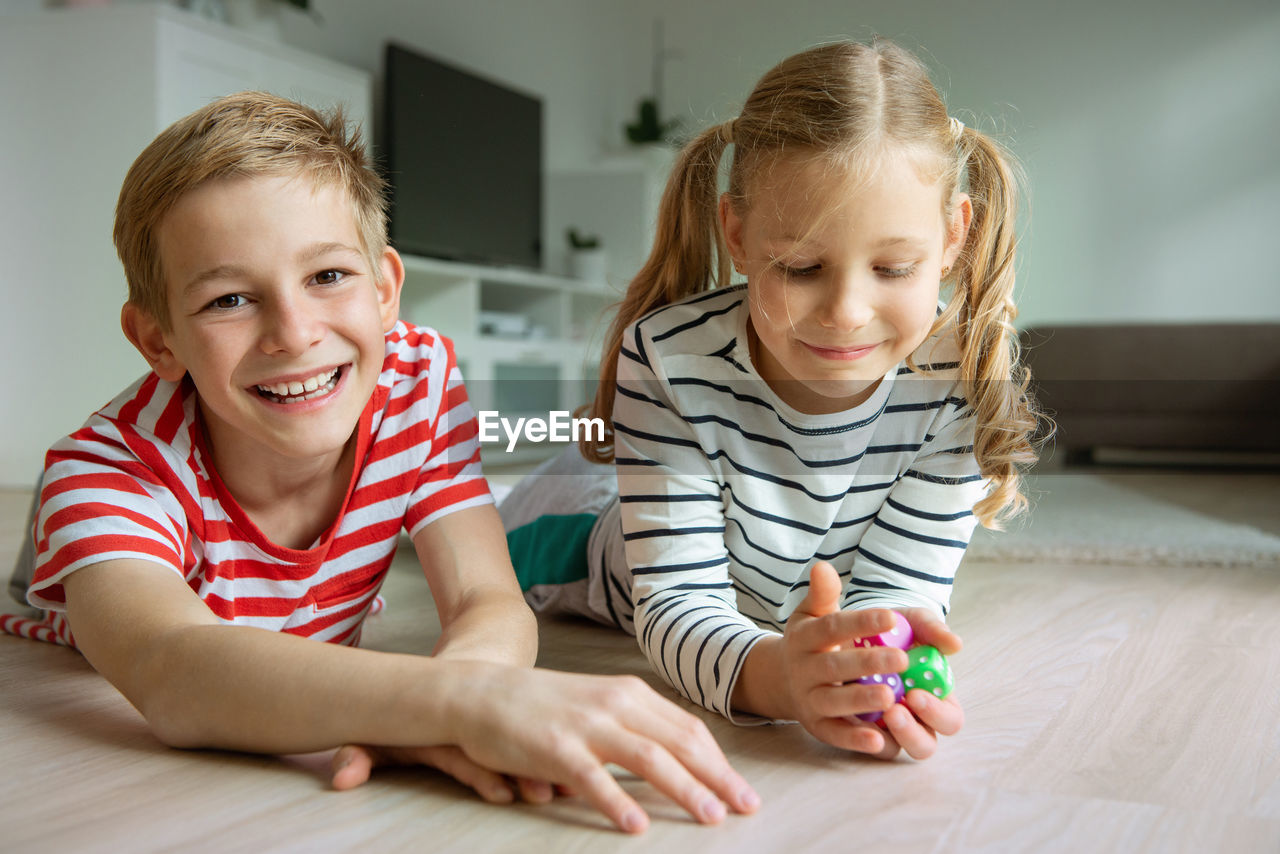 Portrait cheerful siblings playing with dice while lying on carpet at home