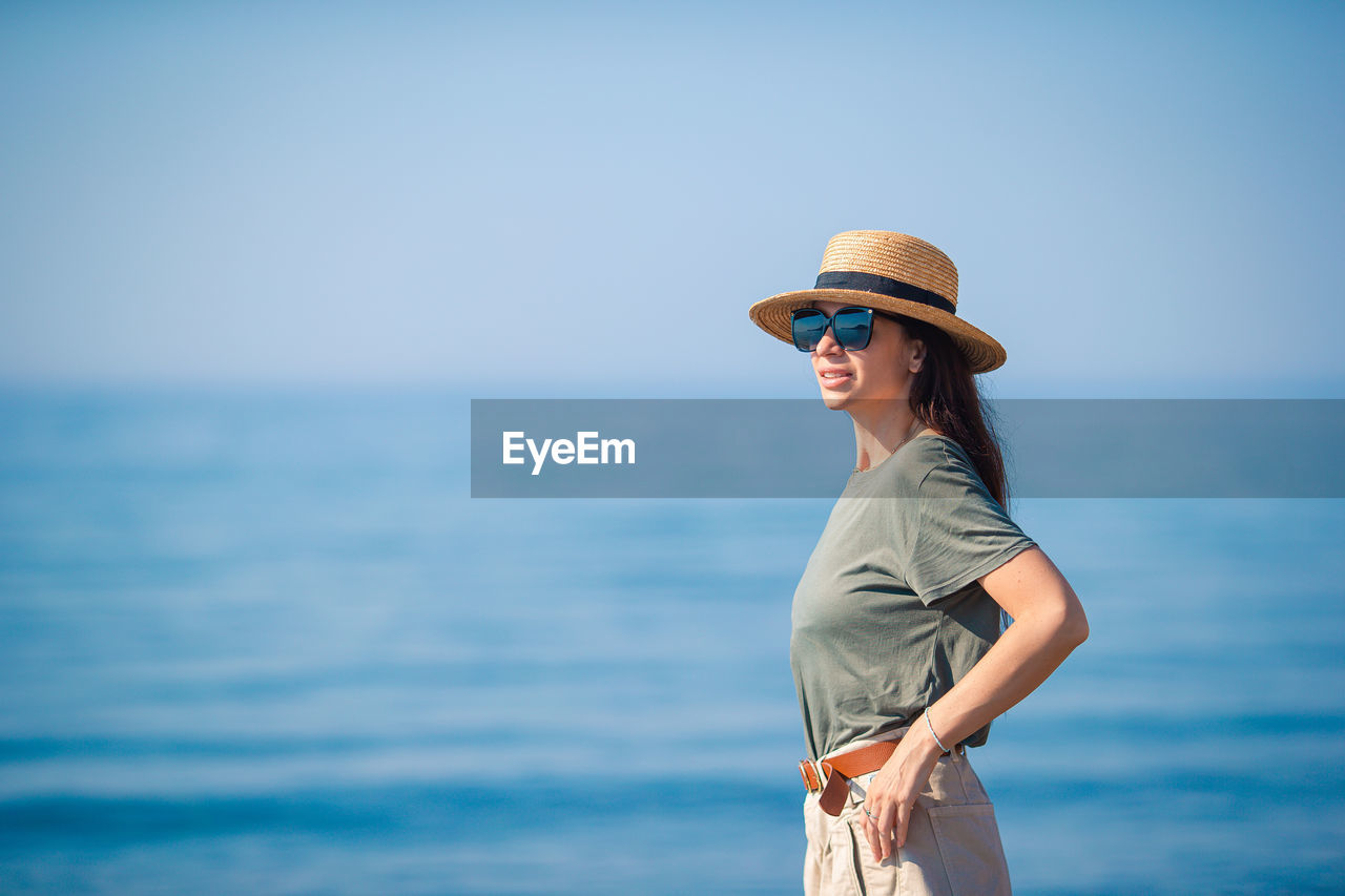 side view of woman wearing hat standing against sea against sky