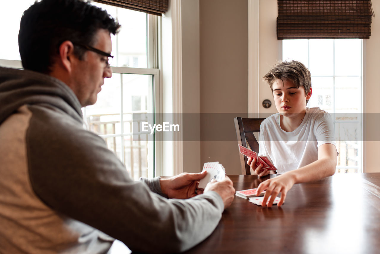 Adolescent boy and his father playing cards at the table together.