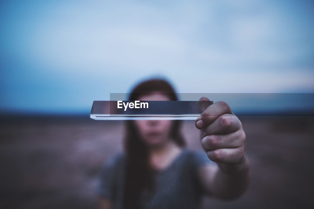 Close-up of woman holding smart phone against sky