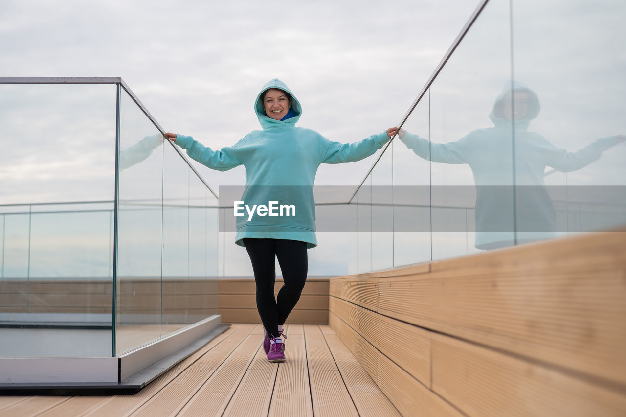 Portrait of woman standing by glass railing against sky