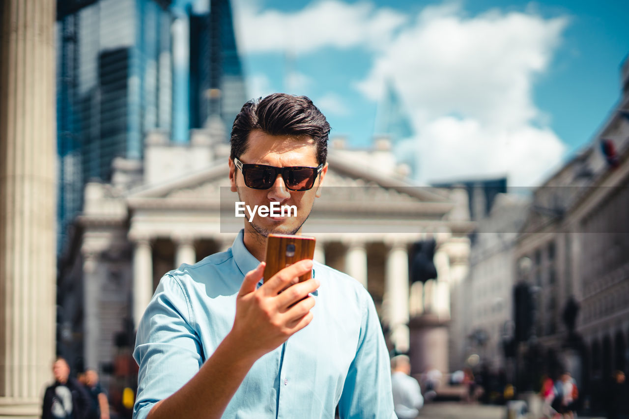 Man using phone while standing against buildings in city