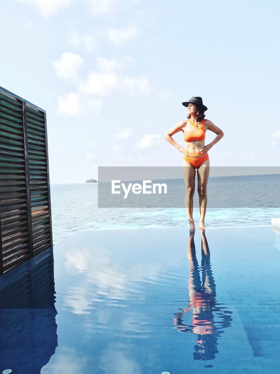 Woman in bikini standing on infinity pool against sky