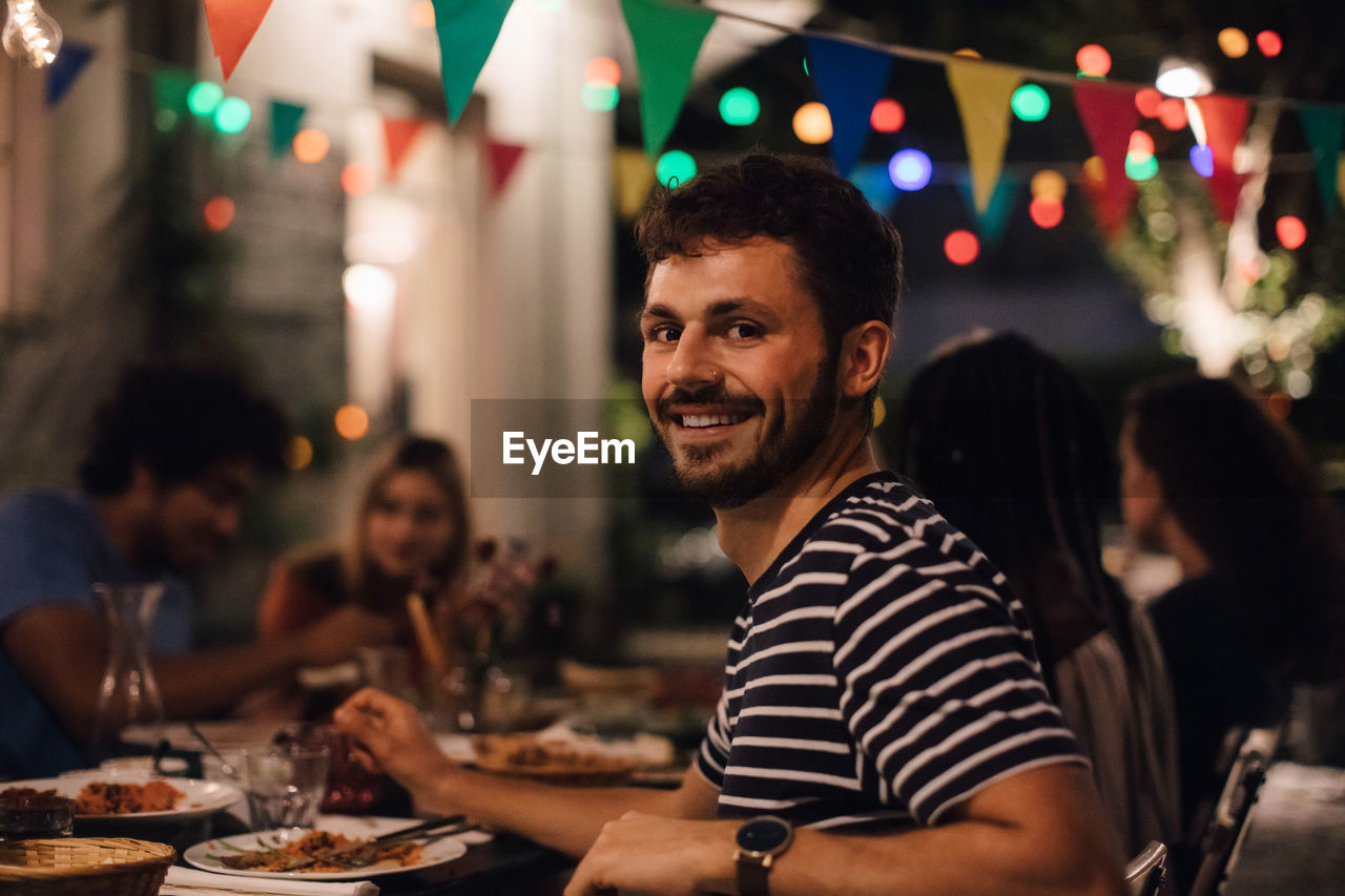 Portrait of smiling young man having dinner with friends during garden party