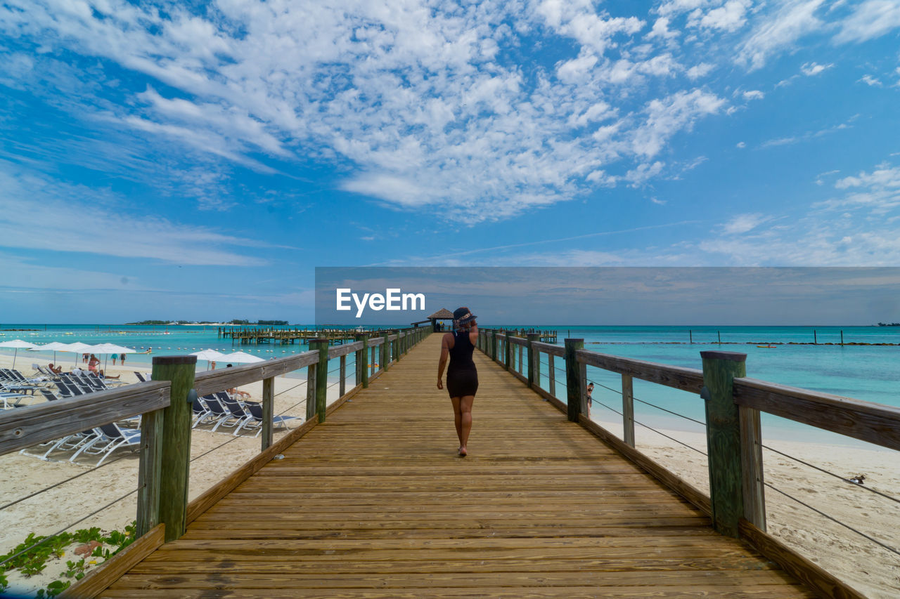 Rear view of woman walking on pier over sea against sky