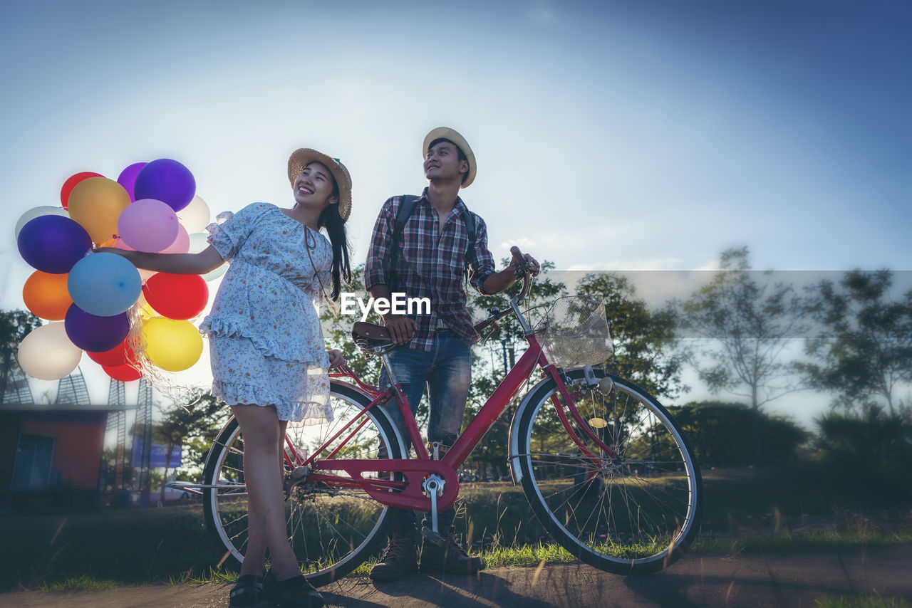 YOUNG COUPLE WITH BICYCLE AGAINST SKY DURING SUNRISE