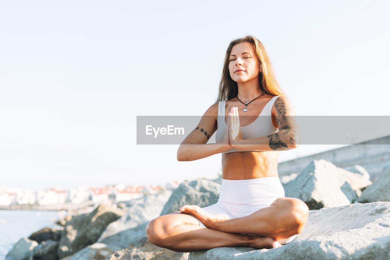Young fit woman with long hair in white sport clothes practice yoga and meditation on sea beach