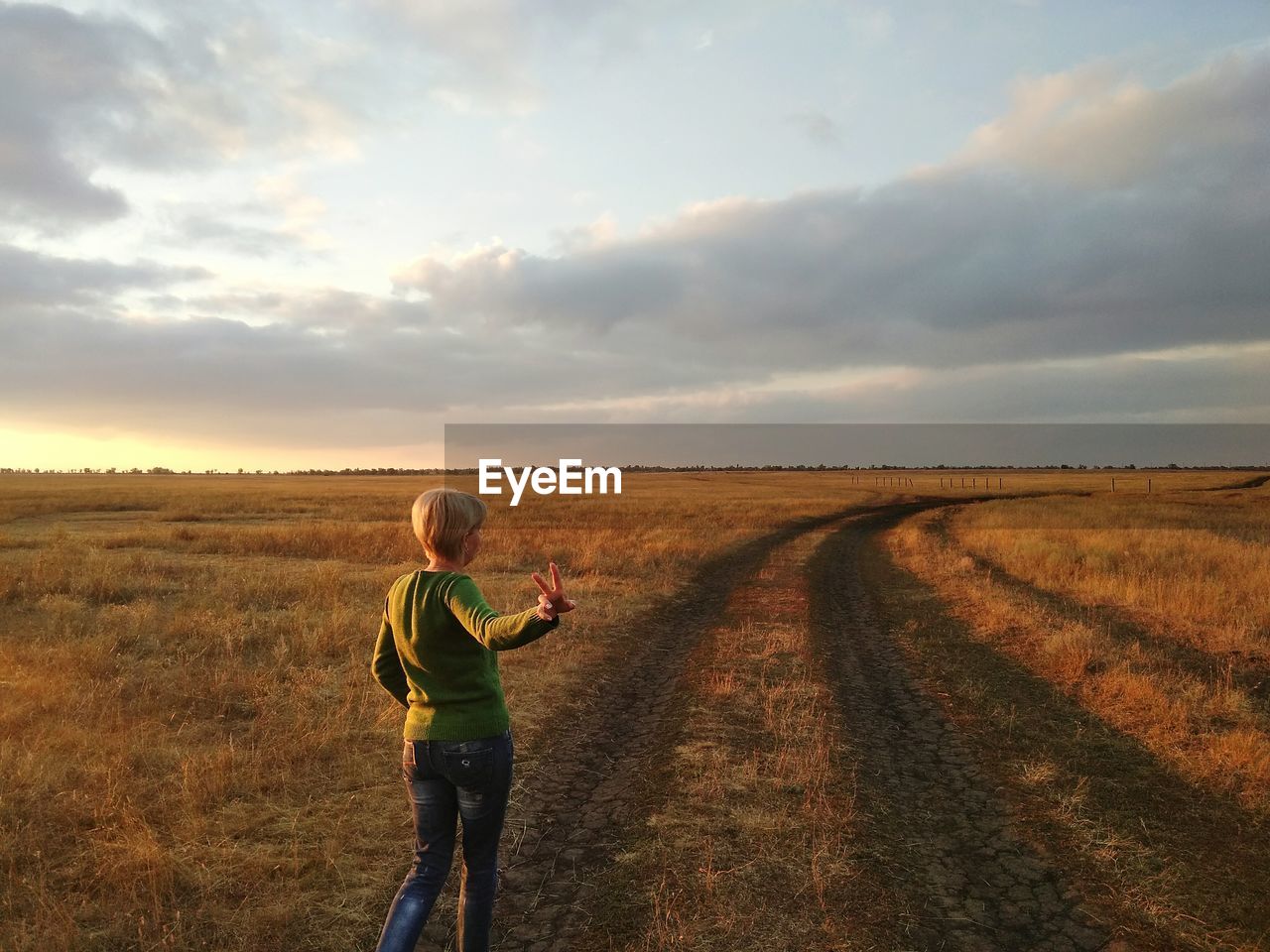 Woman gesturing while walking on grassy field against cloudy sky during sunset