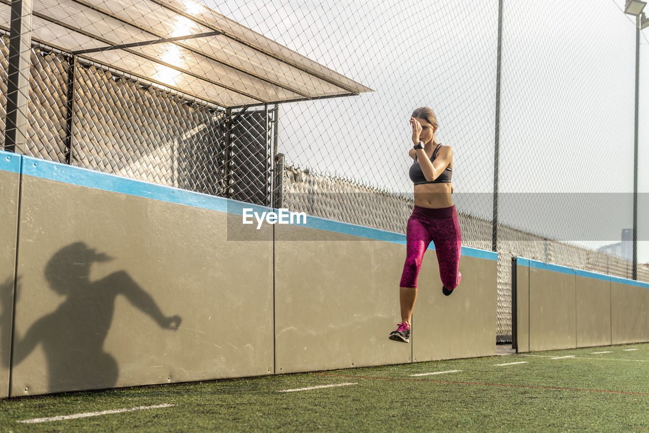 Full body of enduring female athlete in activewear jumping above ground during intense training in stadium