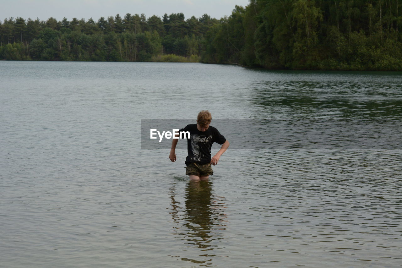 Teenage boy in lake against trees