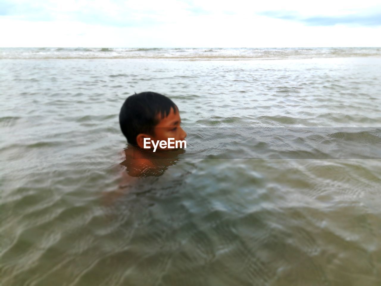 BOY IN SEA AGAINST SKY