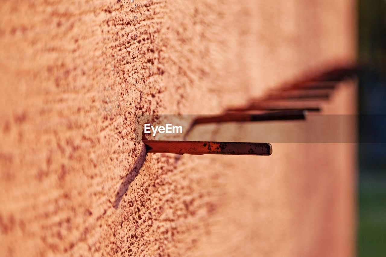 A row of metal sticks protruding from the orange concrete wall may be for defense or assembly