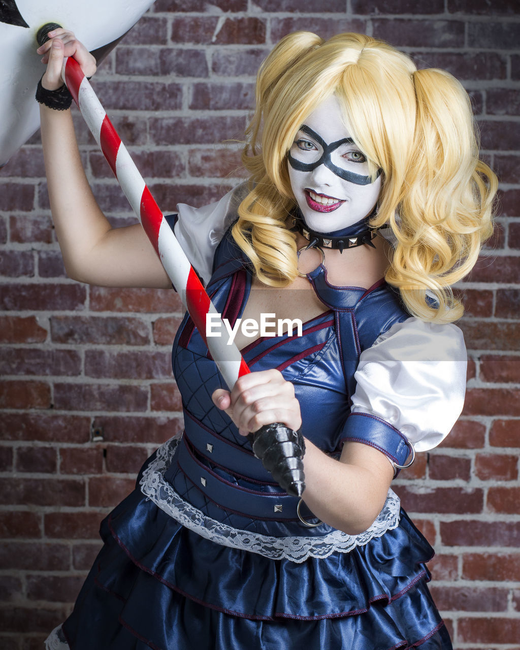 Portrait of smiling young woman with toy wearing costume against brick wall