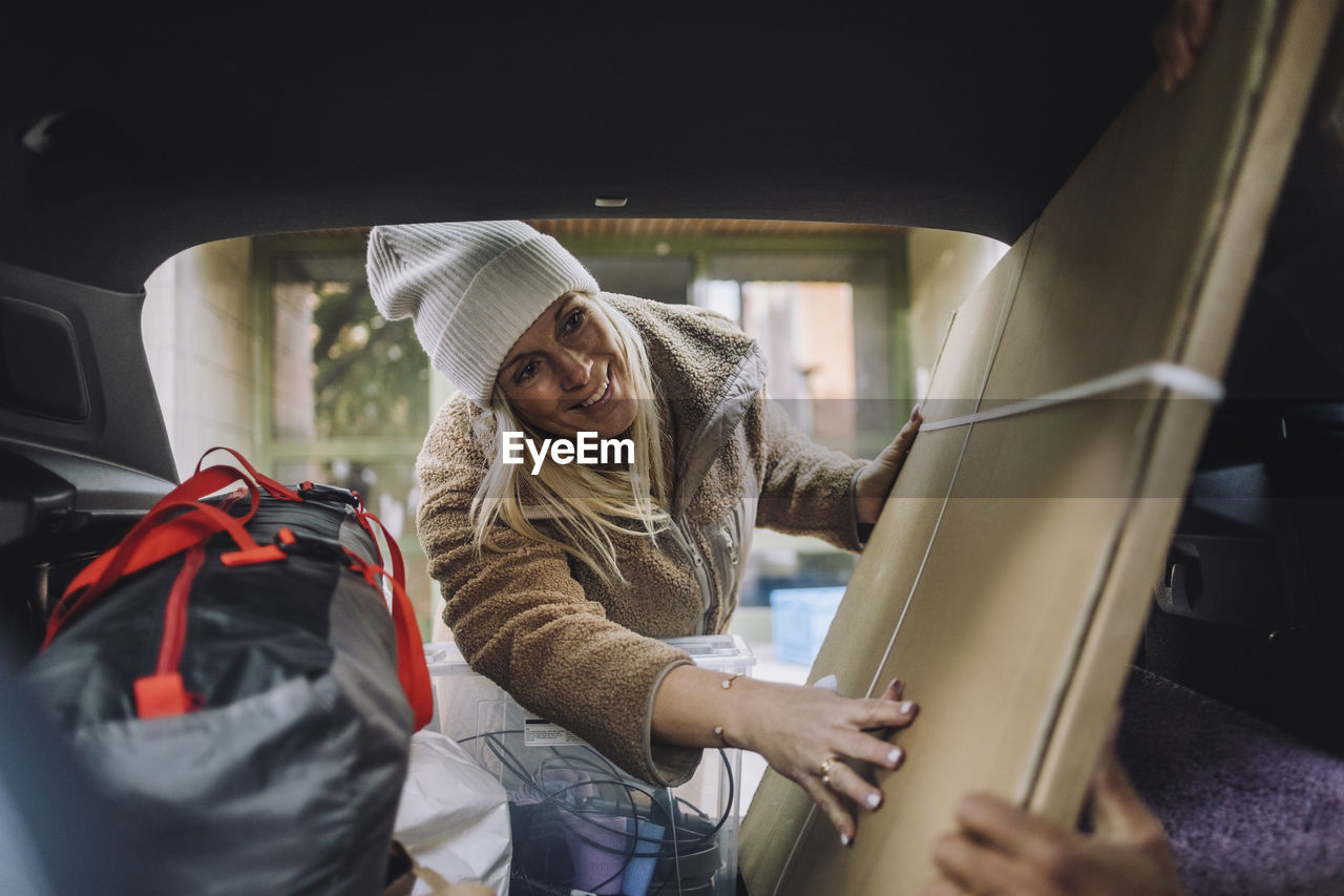 Smiling mature woman loading cardboard in car trunk