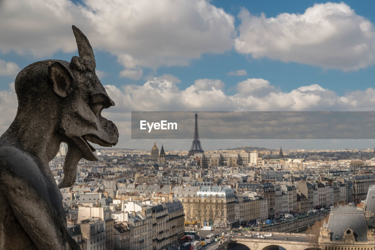 Gargoyle statue in city against sky