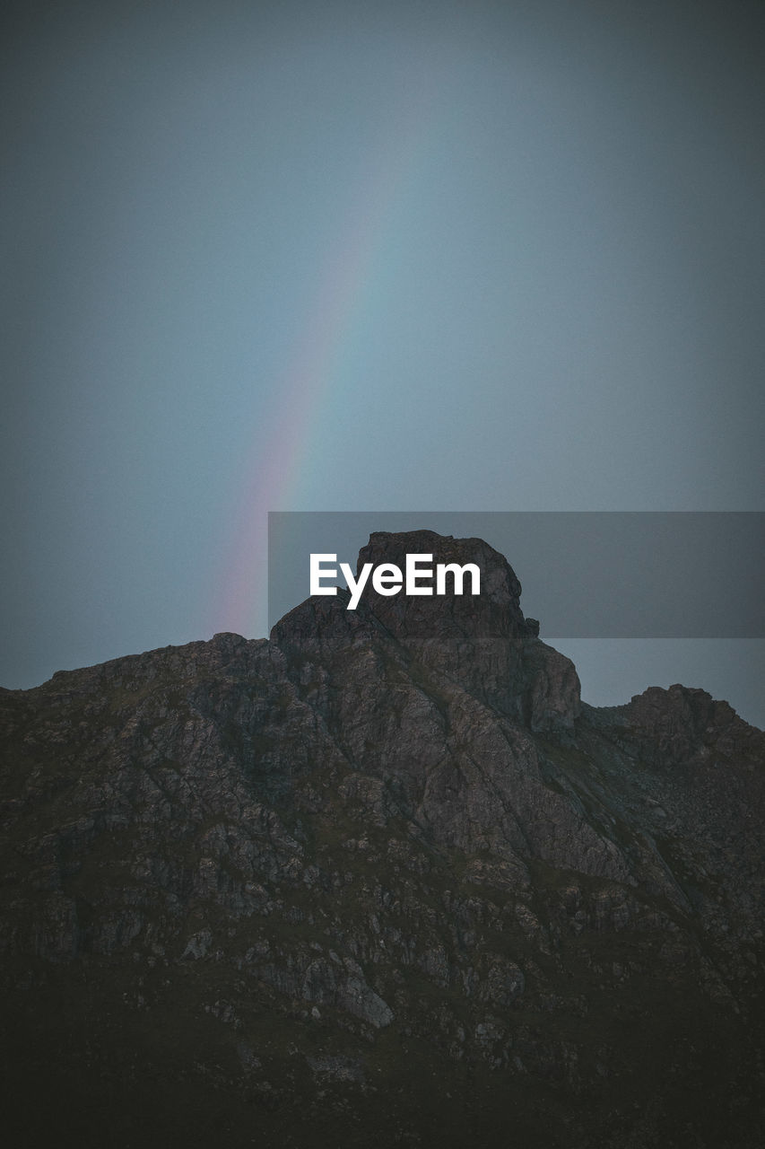 Low angle view of rocky mountain against sky and rainbow