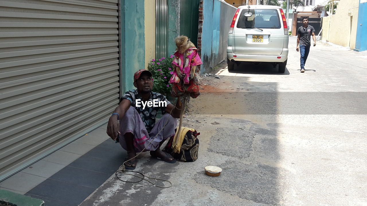 Man holding monkey while crouching on street