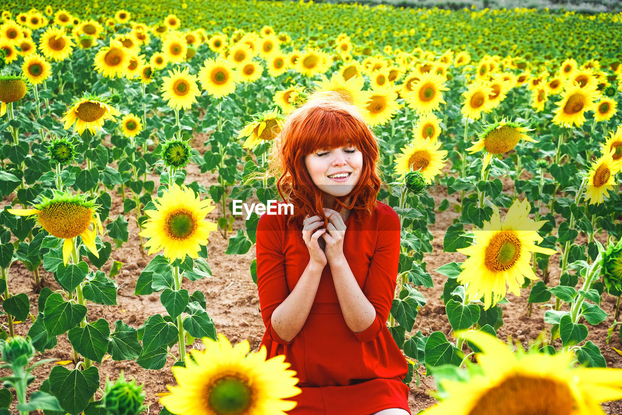 PORTRAIT OF SMILING WOMAN STANDING ON SUNFLOWER