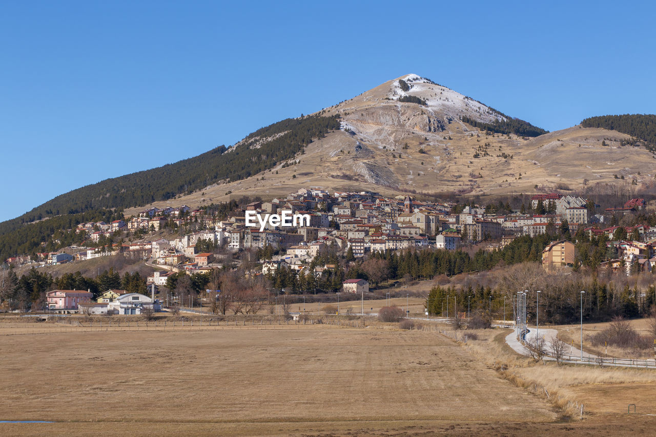 Scenic view of townscape by mountains against clear blue sky