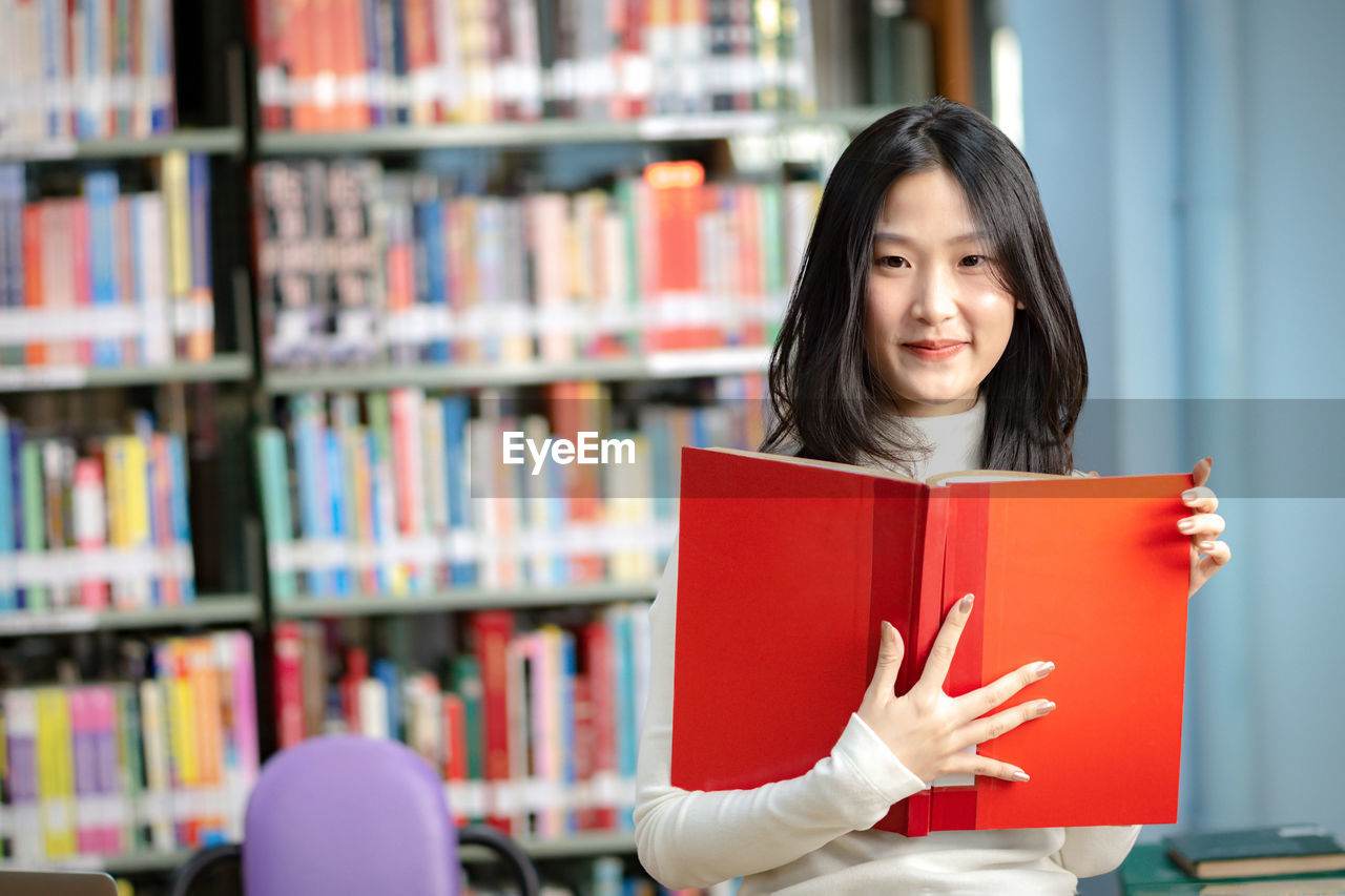 Portrait of smiling young woman reading book in library