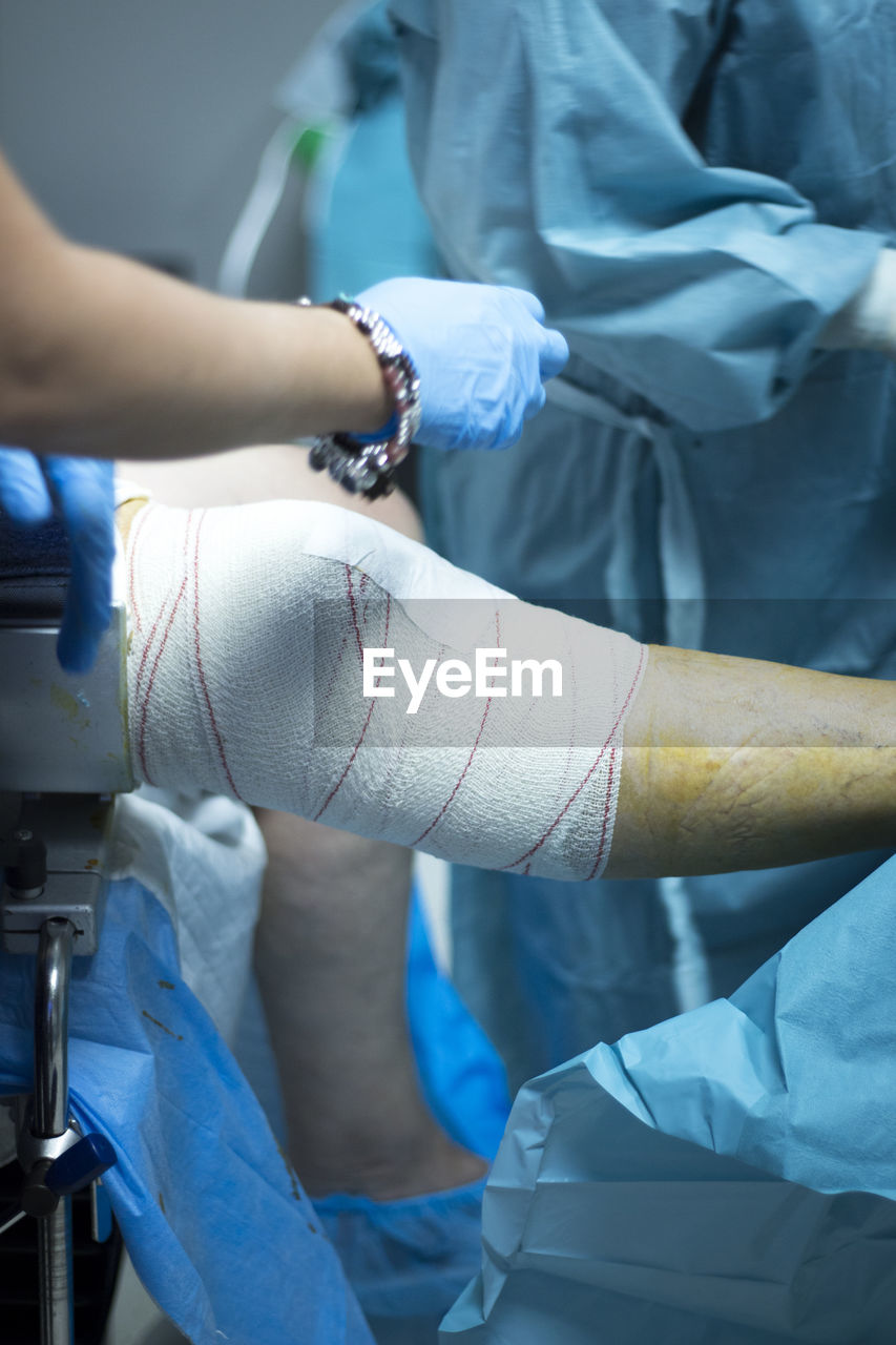 Midsection of surgeon wrapping adhesive bandage on patient leg in hospital