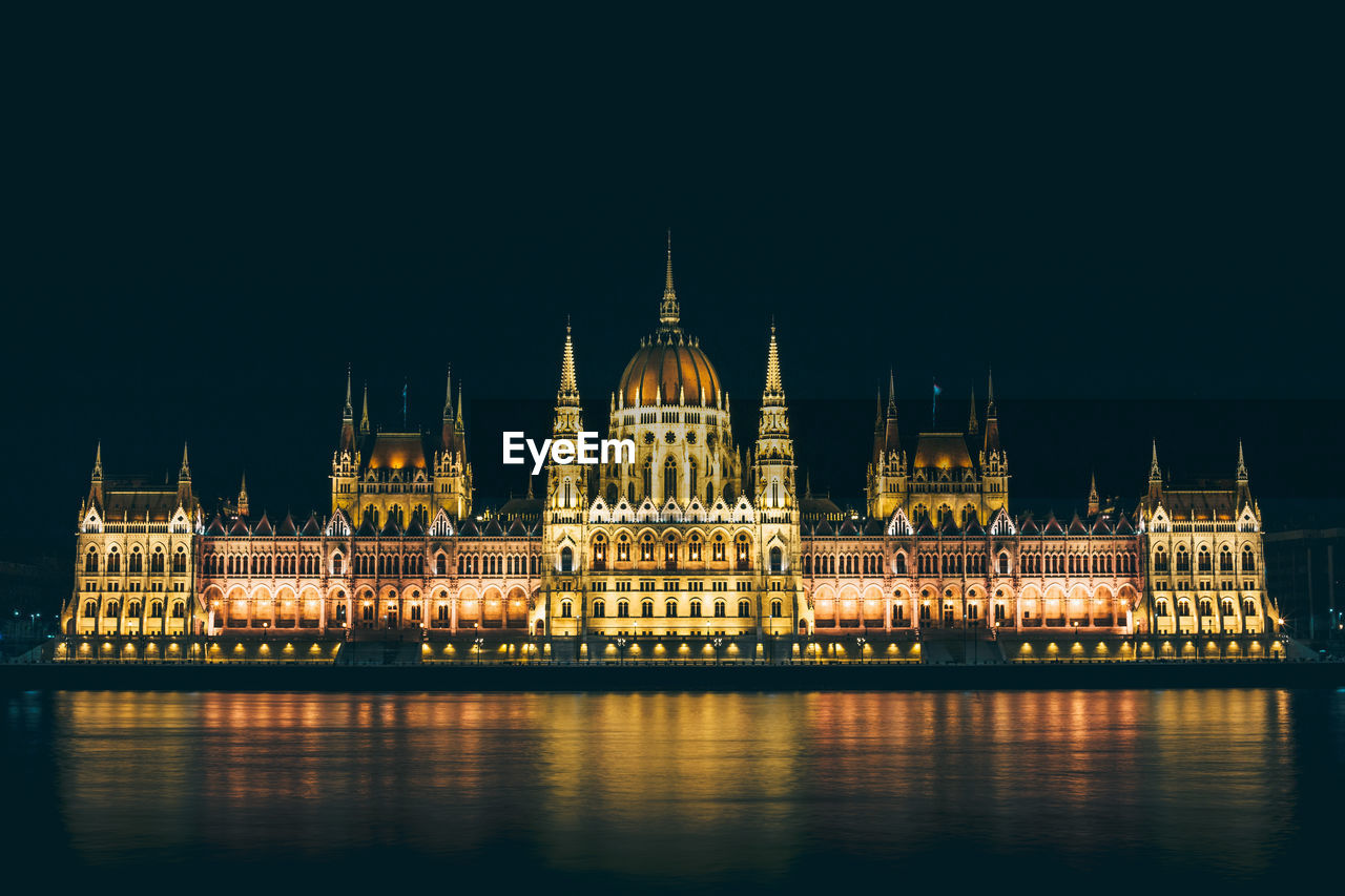 Illuminated hungarian parliament building by river against clear sky at night