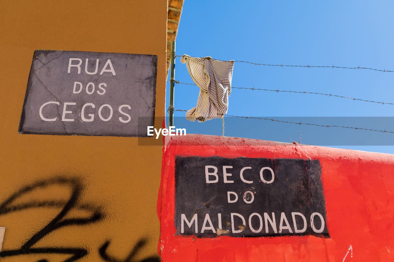 Low angle view of text and graffiti on wall against clear sky