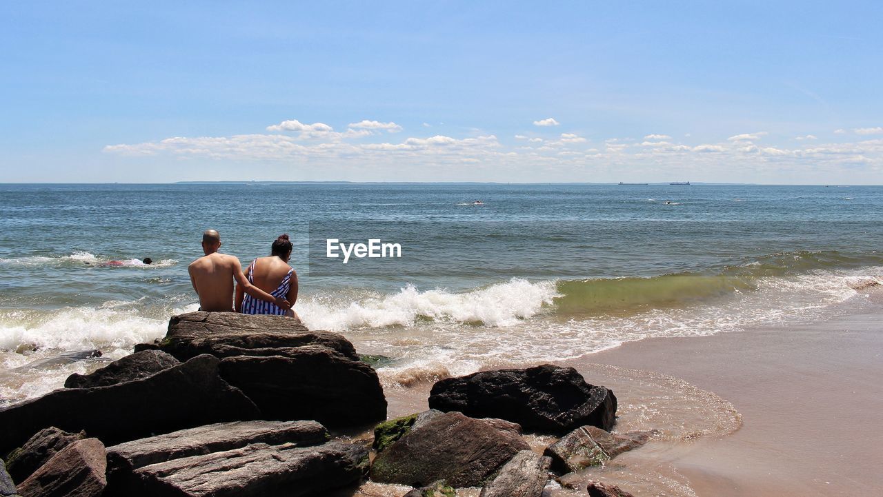 Rear view of man and woman sitting at beach against sky