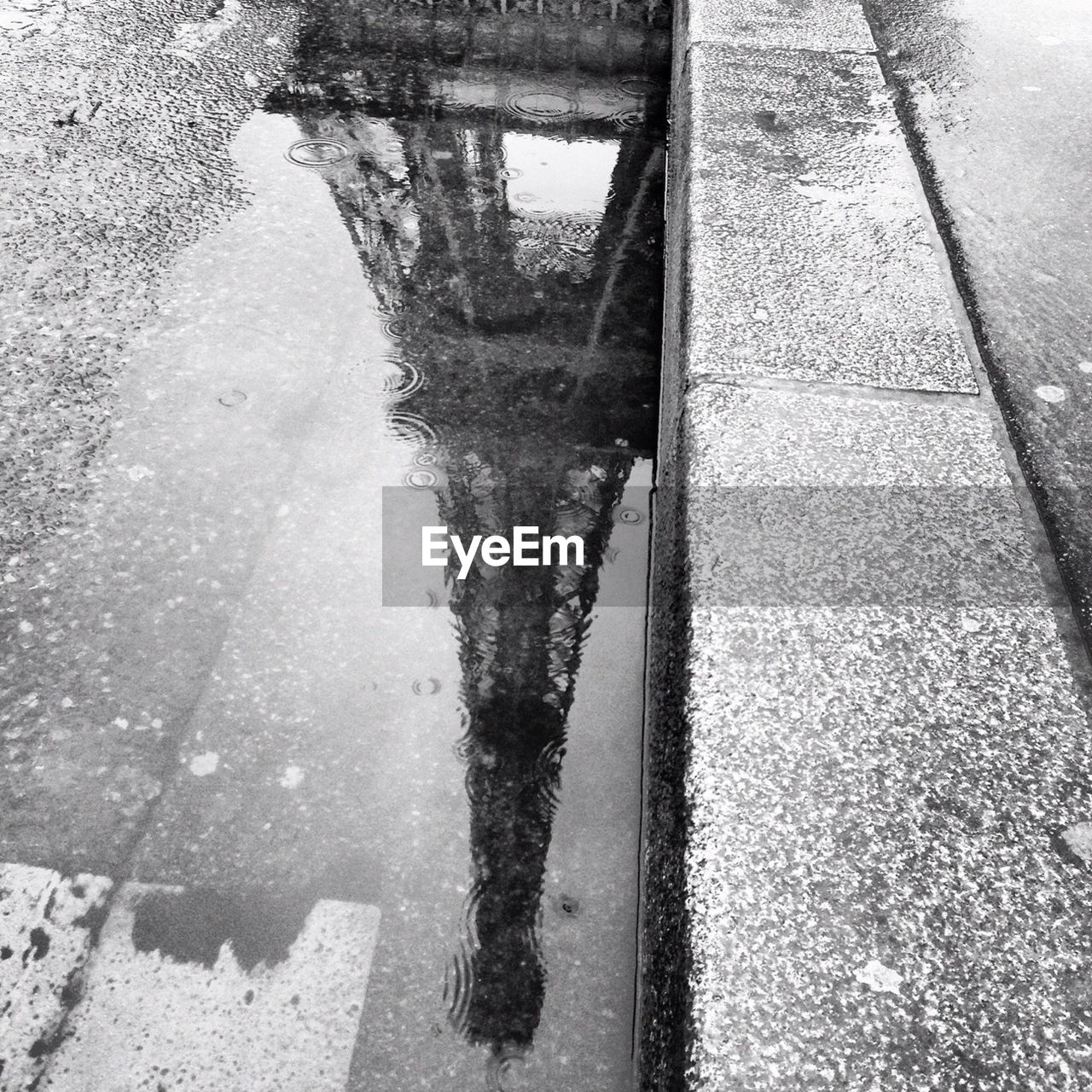 Reflection of eiffel tower in puddle on street during rainy season