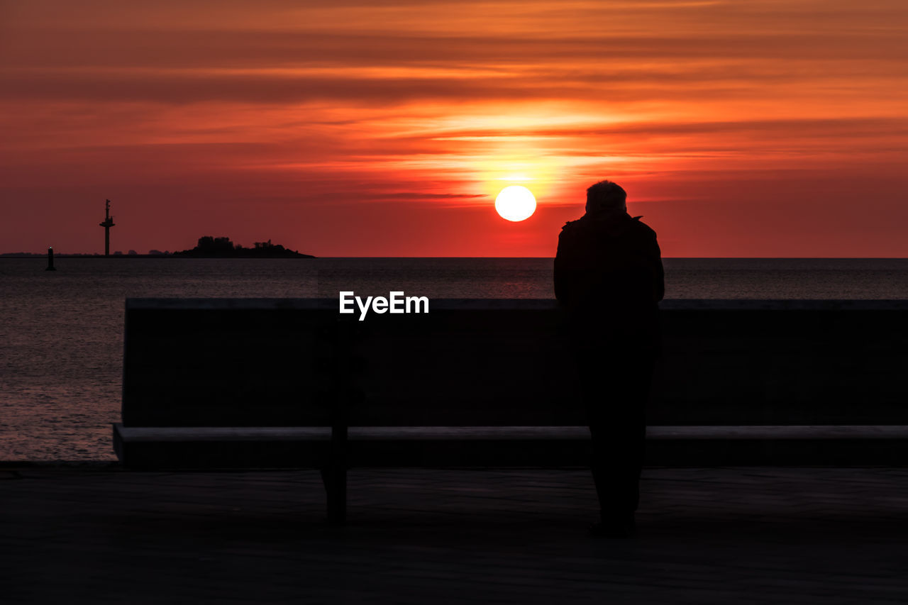 SILHOUETTE MAN ON SEA AGAINST ORANGE SUNSET SKY