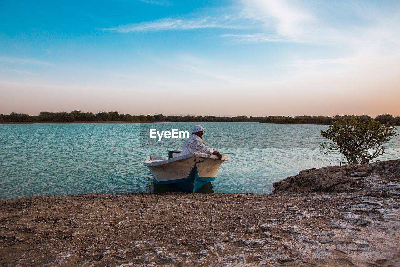 Man sitting on boat in lake against sky