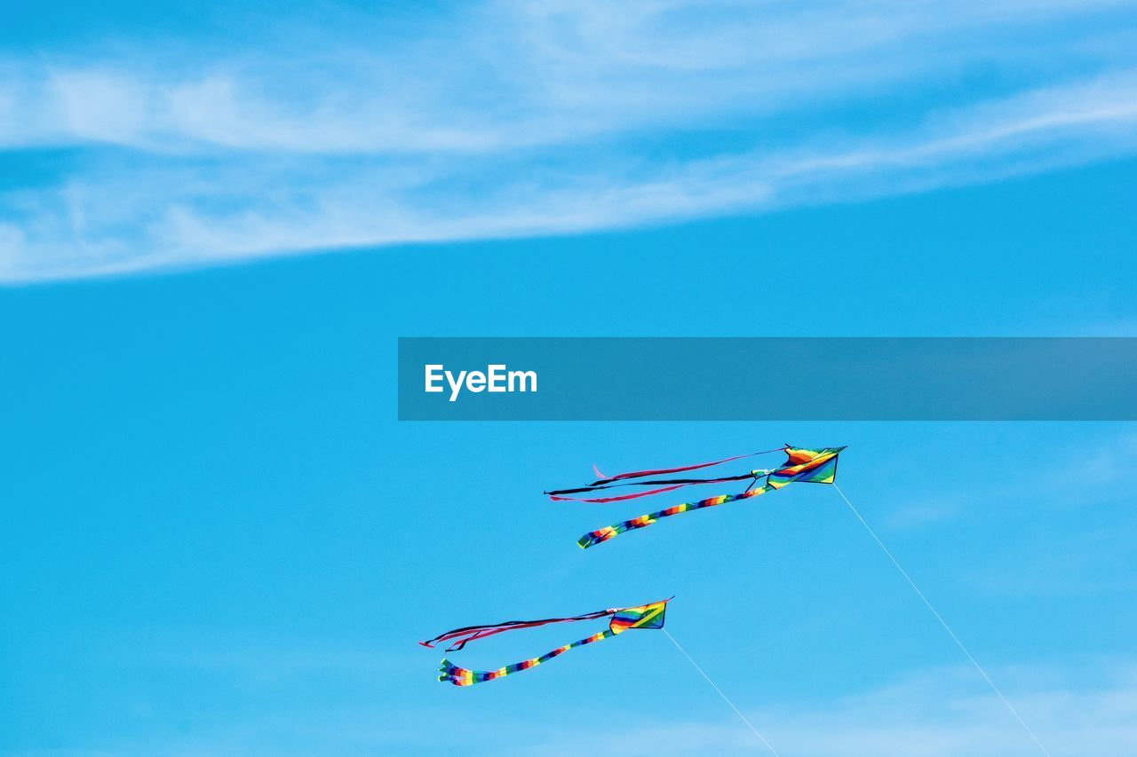 Low angle view of kites flying against blue sky