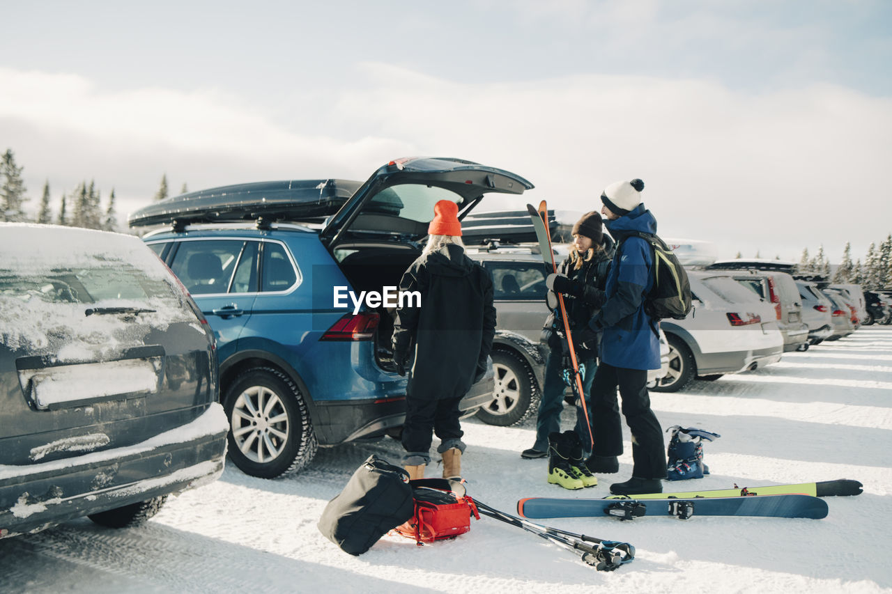 Female and male friends loading skis in trunk car during winter