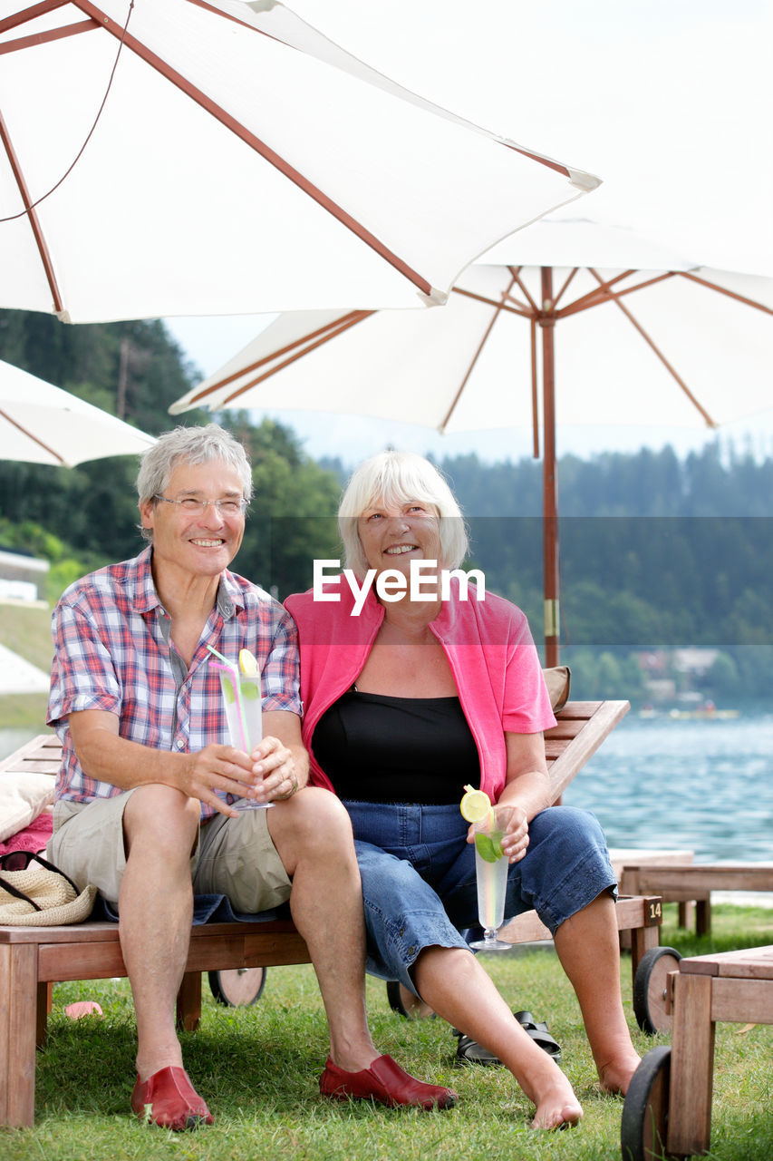 Portrait of senior couple sitting against lake at resort