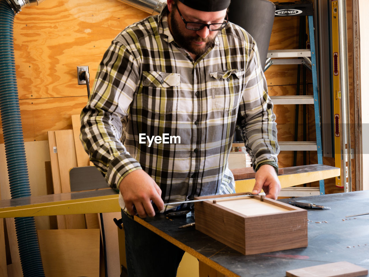 A carpenter measuring the bottom of the box he is building in his woodshop