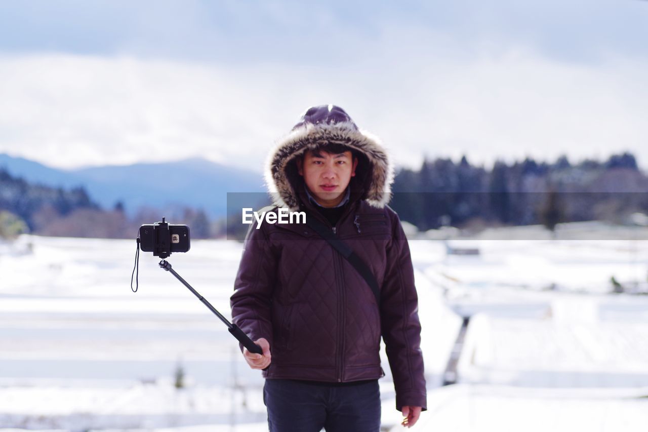 PORTRAIT OF YOUNG WOMAN STANDING ON SNOW COVERED MOUNTAIN