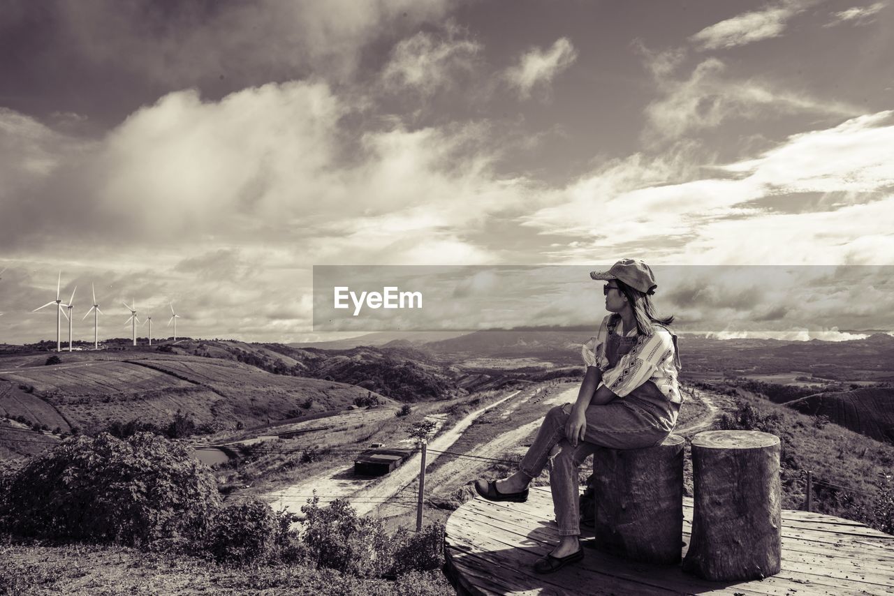 Woman sitting on tree stump on field against sky