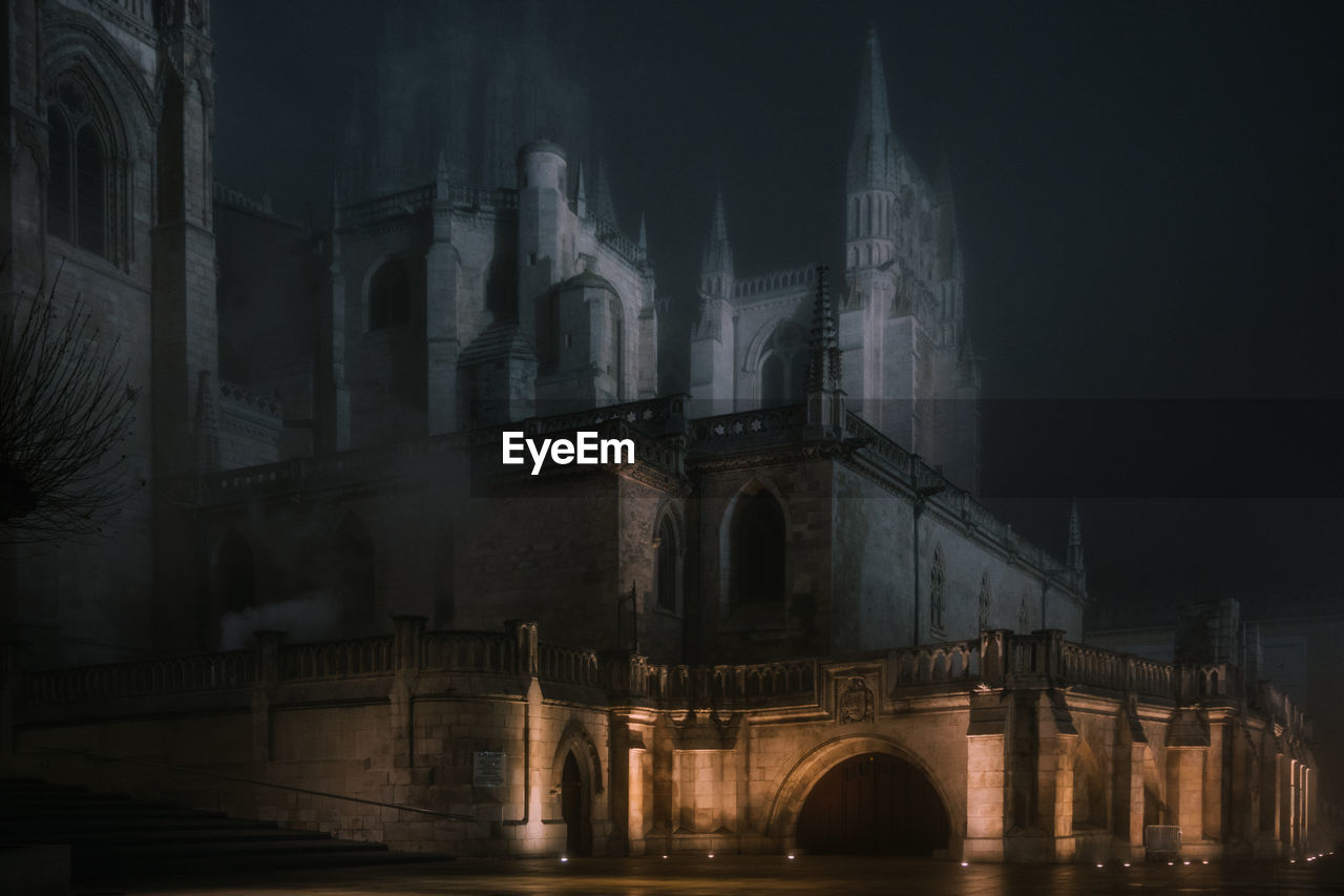 Illuminated stone fence around ancient cathedral building at dark misty night in burgos, spain