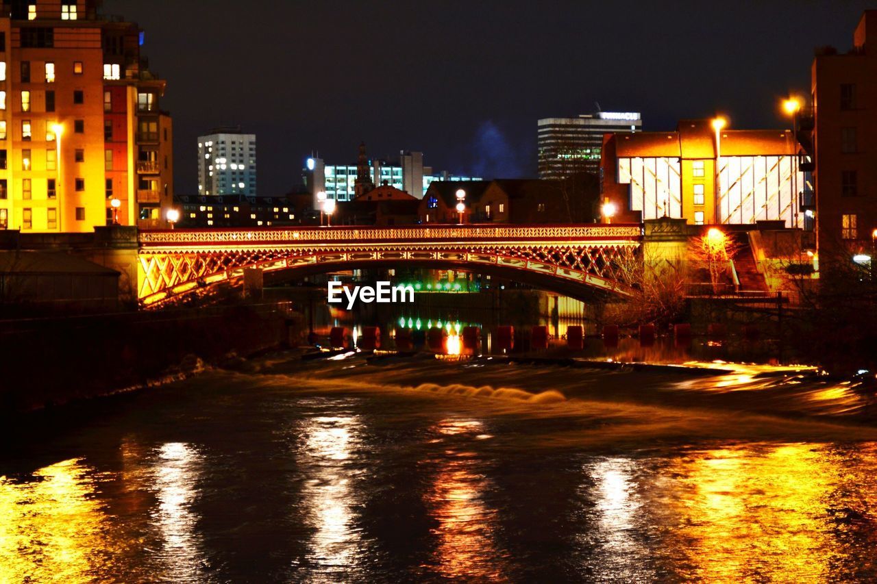 ILLUMINATED BRIDGE OVER RIVER AT NIGHT