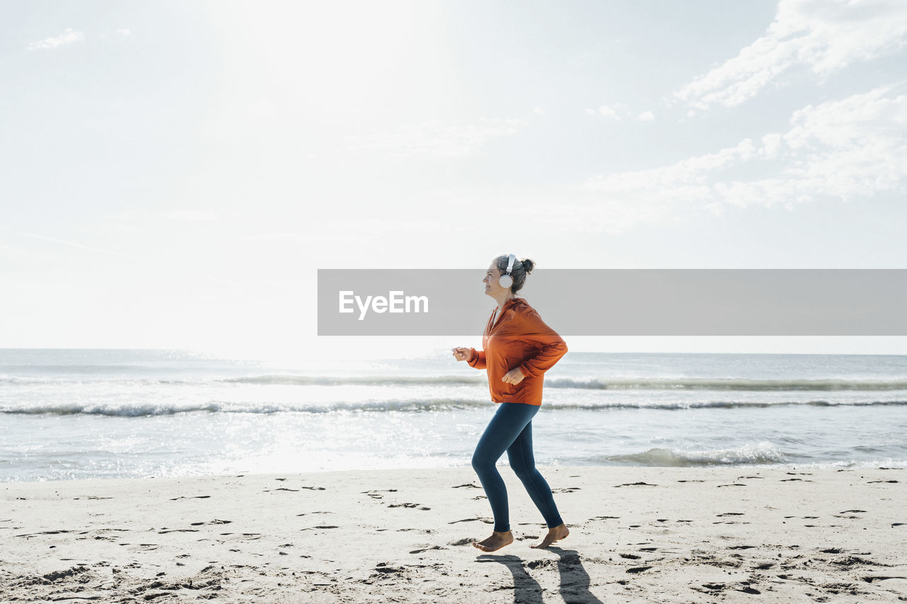 Mature woman wearing headphones jogging at beach