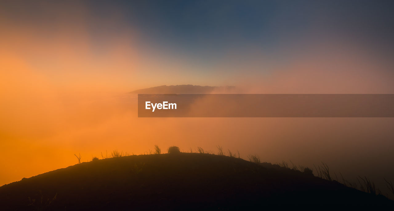 Magnificent view of grassy hill surrounded by thick mist at sundown in highland area