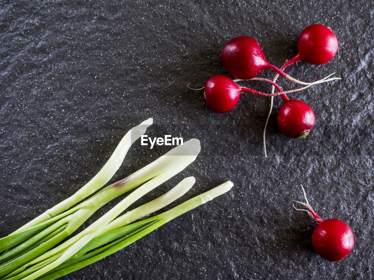 Directly above shot of radishes by scallions on slate