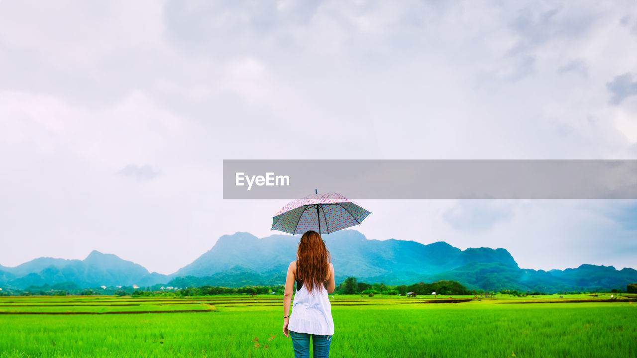 rear view of woman standing on field against cloudy sky