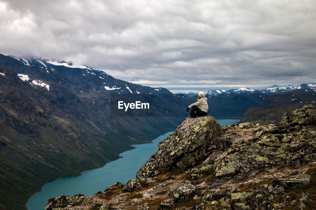 Man sitting on rock by mountains against sky