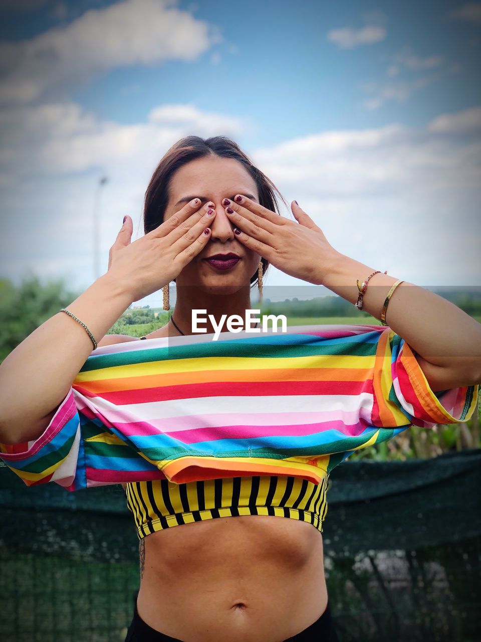 Young woman with hands covering eyes against sky